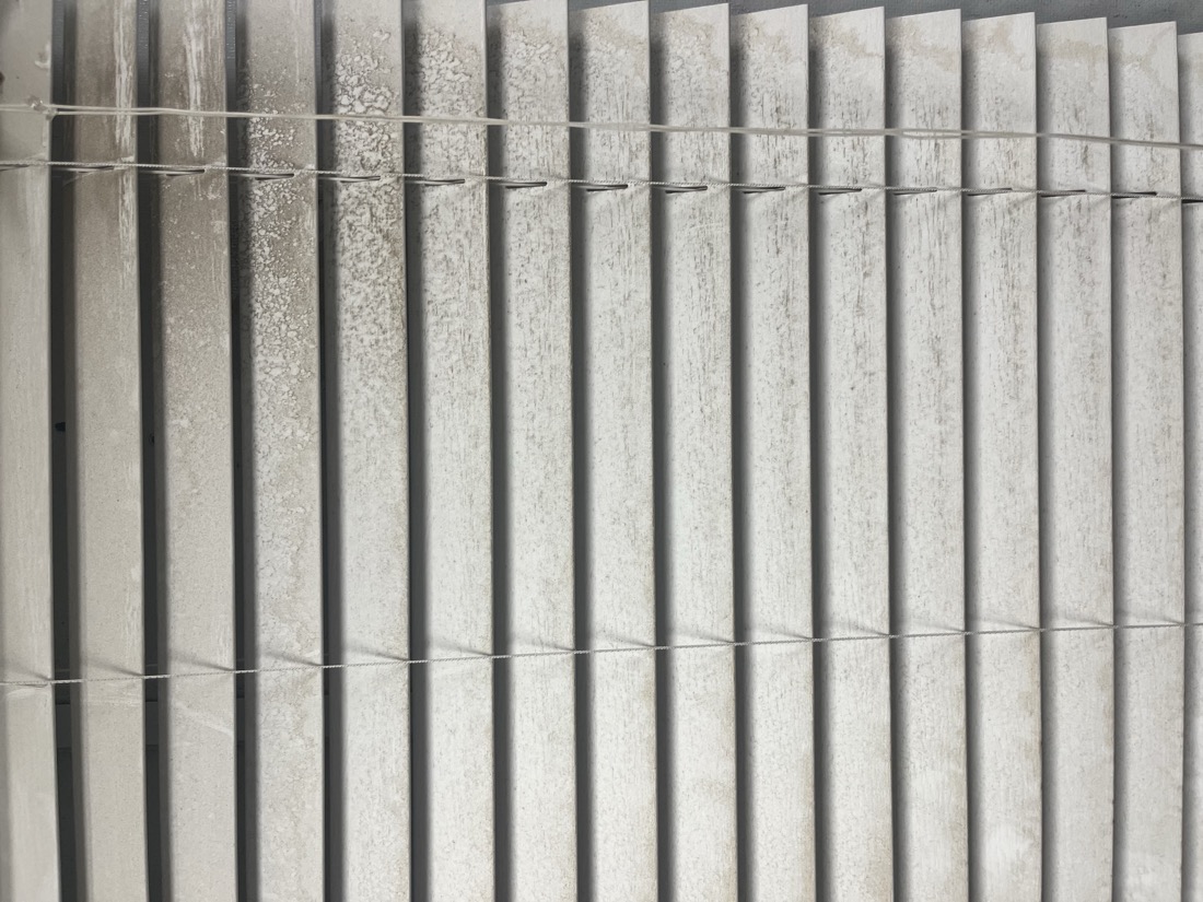 Grimy, dusty vertical blinds with water spots before cleaning